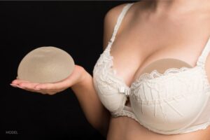 woman in a white bra holding a silicone implant in her palm.