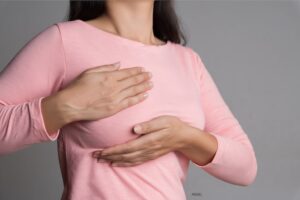 Woman cupping her breast over a pink shirt.