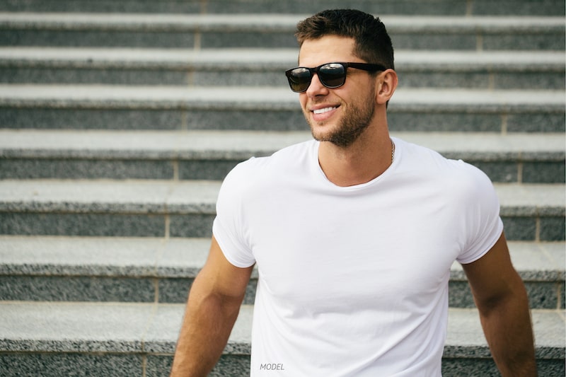 Young, fit man wearing sunglasses leaning against stairs. 