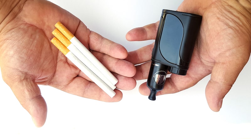 Man's hands holding cigarettes and vape