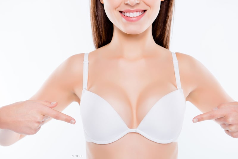 Young woman in bra pointing to breasts.