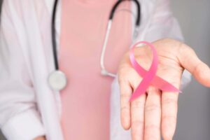 Female doctor holding a pink ribbon for breast cancer in her palm.
